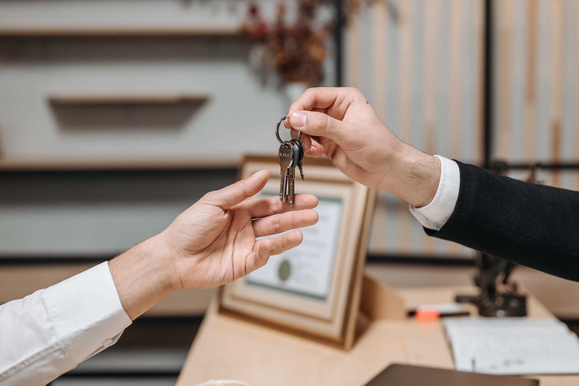 One hand passing a set of keys to another across a desk in a professional office.